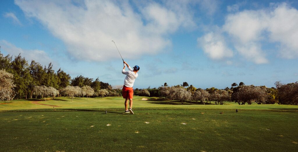 A golfer swings on a picturesque golf course with lush greenery and a clear blue sky, epitomizing outdoor leisure.